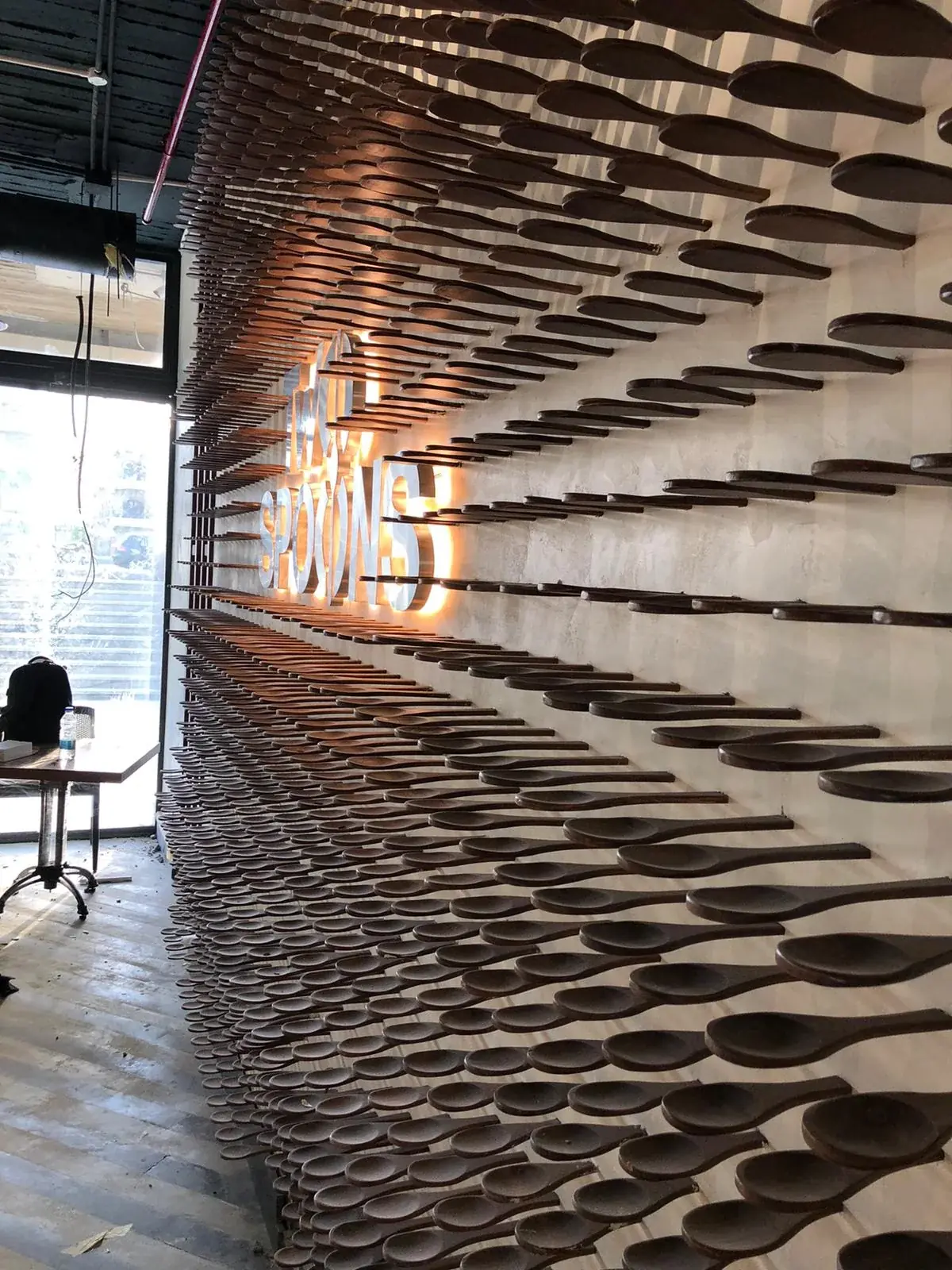 Side view of the illuminated Two Spoons sign within the sculptural spoon wall