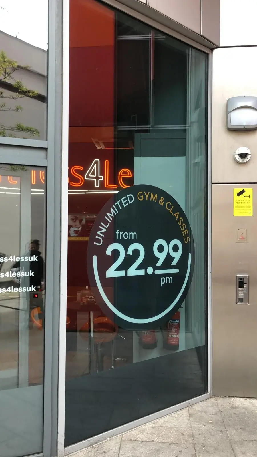 Gym membership offer window vinyl on a tall pane at the Fitness4Less entrance