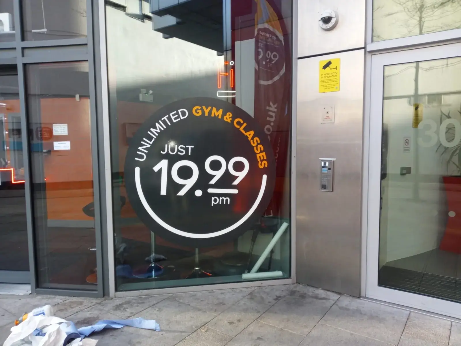 Fitness4Less promotional window vinyl during installation beside the entrance