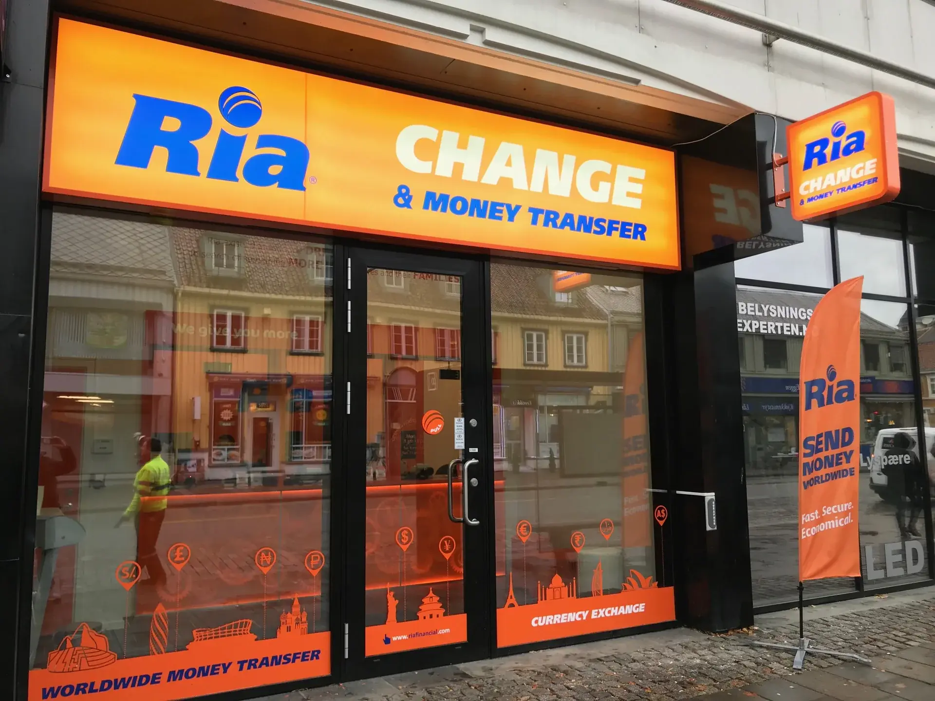 Ria Money Transfer shopfront with illuminated fascia sign, projecting sign and orange window graphics