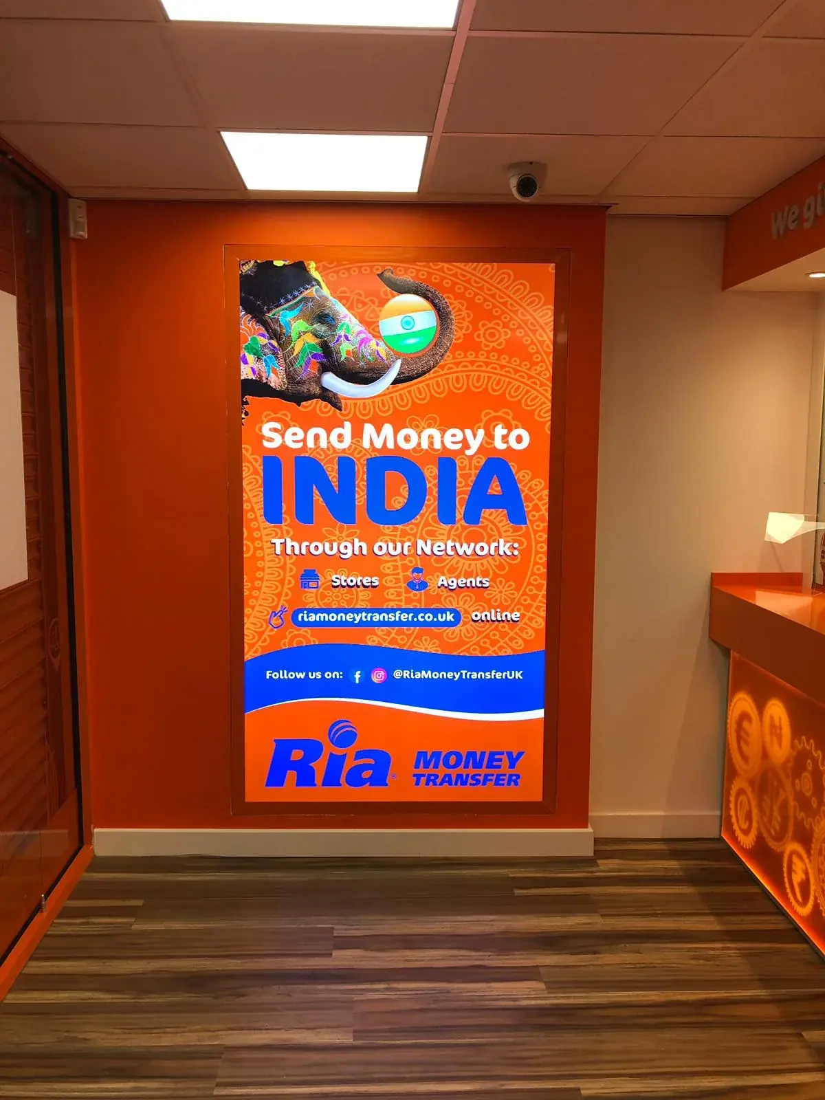 Illuminated Ria Send Money to India campaign display inside the branch