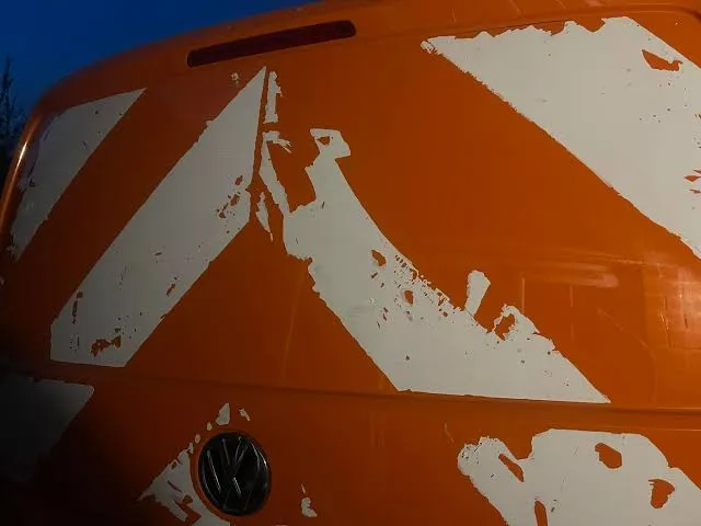 Red-orange van rear panel with large irregular pale areas where the coloured surface coating is missing