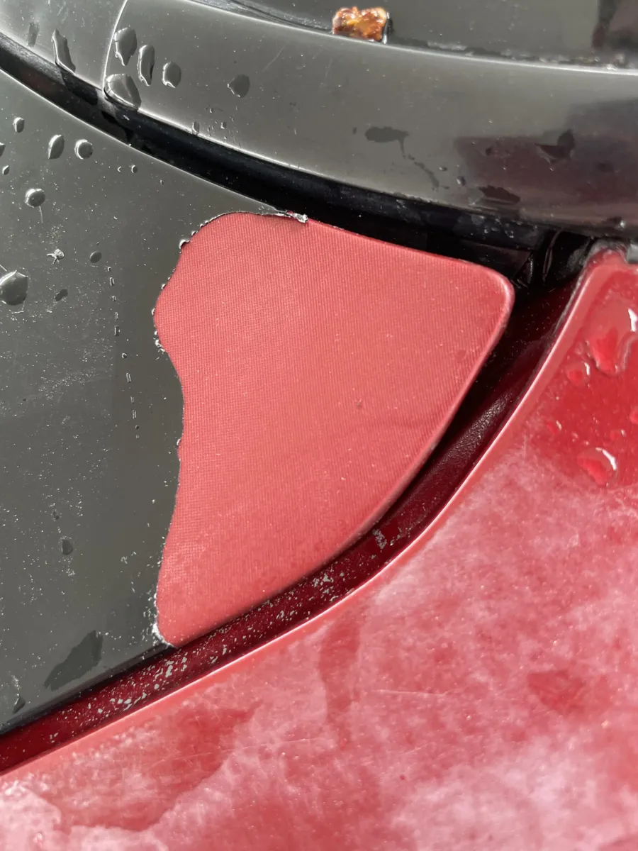 Close-up of peeling dark surface coating exposing red bodywork beneath